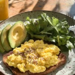 Breakfast plate with scrambled eggs, avocado, toast, and sunflower seeds.